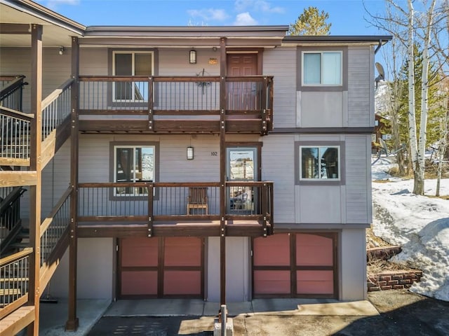 rear view of house with a garage, driveway, stairs, and a balcony
