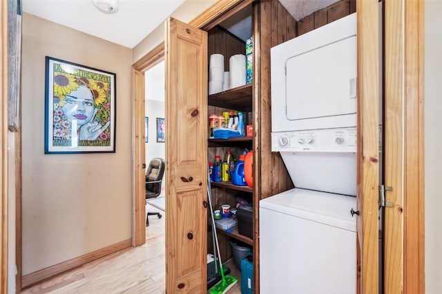 washroom with baseboards, wood finished floors, stacked washing maching and dryer, and laundry area