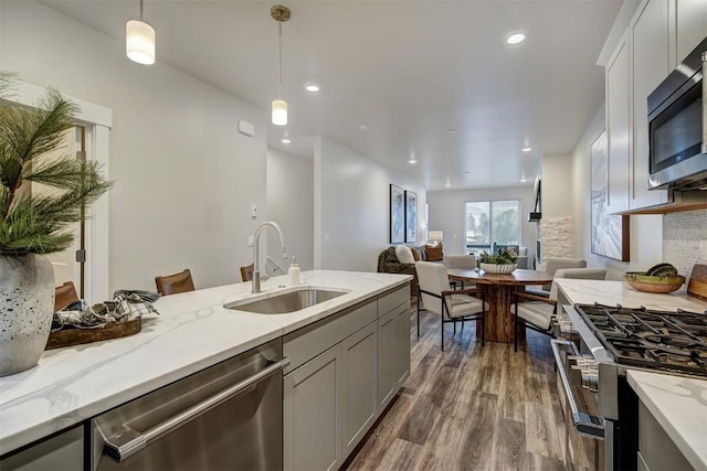 kitchen featuring dark wood finished floors, light stone counters, a sink, hanging light fixtures, and appliances with stainless steel finishes