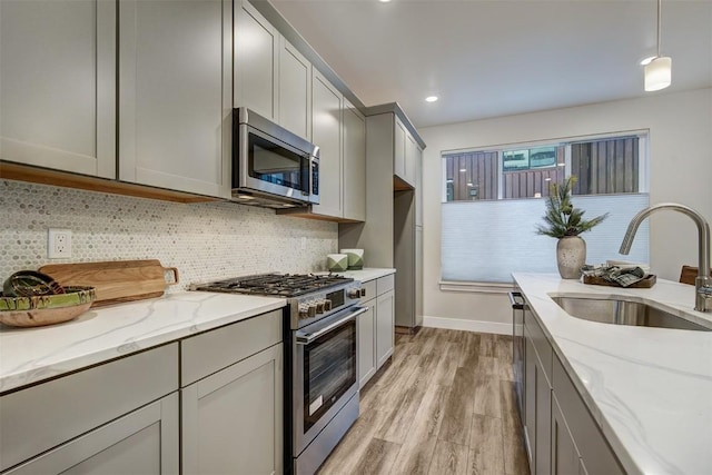 kitchen with a sink, light wood-style floors, gray cabinetry, light stone counters, and appliances with stainless steel finishes