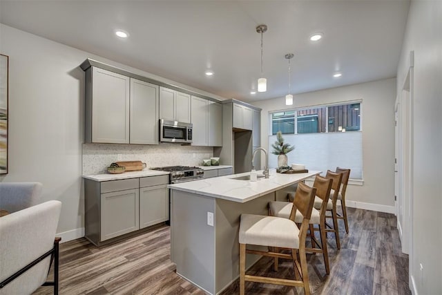 kitchen with backsplash, gray cabinets, a sink, appliances with stainless steel finishes, and dark wood-style flooring
