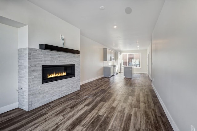 unfurnished living room with recessed lighting, a stone fireplace, dark wood-type flooring, and baseboards
