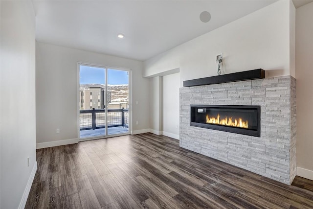 unfurnished living room with wood finished floors, baseboards, and a stone fireplace