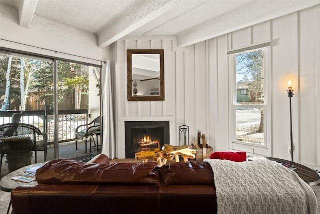living room with beamed ceiling, a decorative wall, a large fireplace, and a wealth of natural light