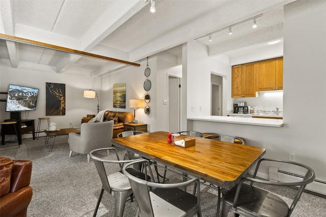 carpeted dining room with beamed ceiling and track lighting