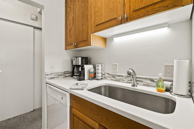 kitchen featuring a sink, backsplash, white dishwasher, brown cabinets, and light countertops