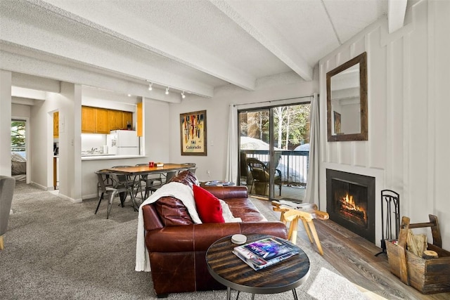 carpeted living area with beam ceiling, baseboards, a wealth of natural light, and a warm lit fireplace