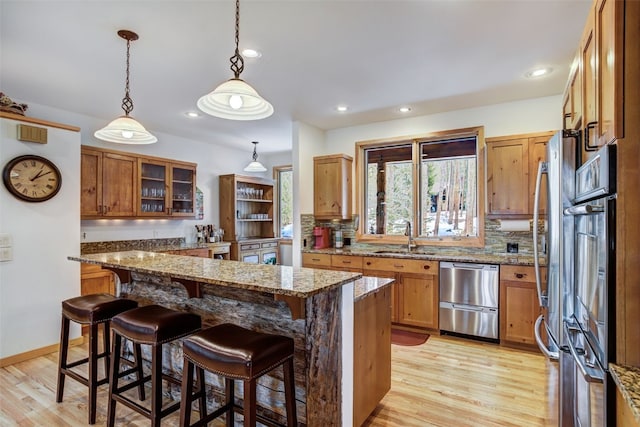 kitchen with a breakfast bar, a sink, light wood-style floors, dishwasher, and backsplash