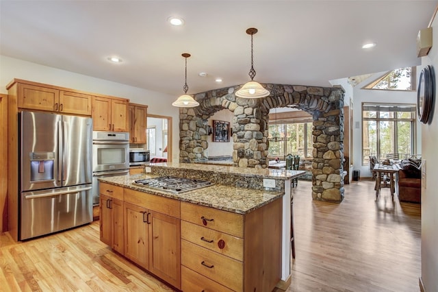 kitchen with light wood-type flooring, light stone counters, a center island, and stainless steel appliances