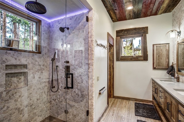 bathroom with a sink, double vanity, baseboards, wood finished floors, and a stall shower