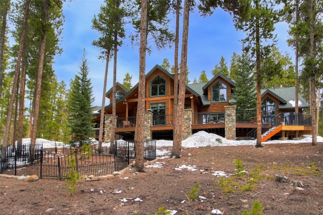 rear view of property featuring fence, stone siding, and a deck