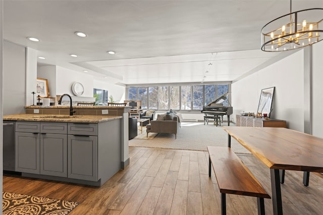 kitchen featuring an inviting chandelier, wood finished floors, gray cabinets, a sink, and open floor plan