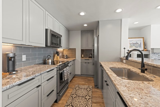 kitchen featuring light stone countertops, a sink, backsplash, and appliances with stainless steel finishes