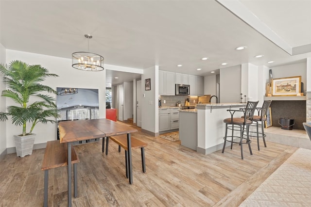 kitchen featuring recessed lighting, stainless steel microwave, light wood-style floors, tasteful backsplash, and a breakfast bar area