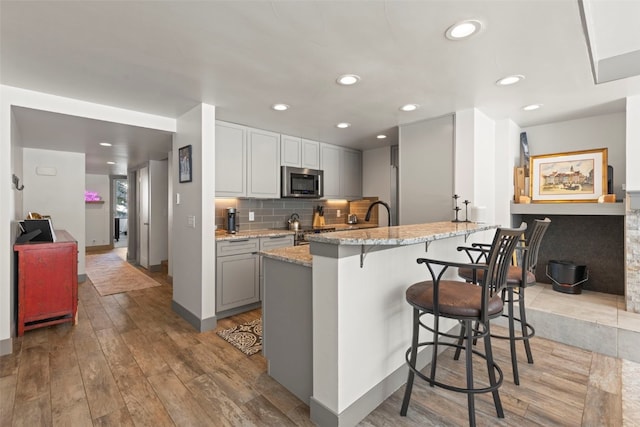 kitchen with light wood-style floors, a breakfast bar area, stainless steel microwave, a peninsula, and light stone countertops