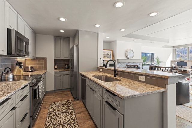 kitchen with a sink, open floor plan, a peninsula, appliances with stainless steel finishes, and gray cabinetry