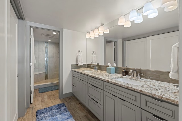 bathroom featuring a tile shower, wood finished floors, decorative backsplash, and a sink