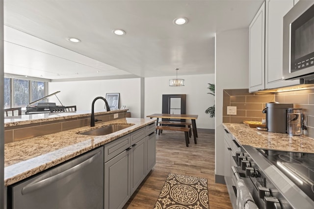 kitchen featuring dark wood-style floors, a sink, decorative backsplash, light stone counters, and appliances with stainless steel finishes