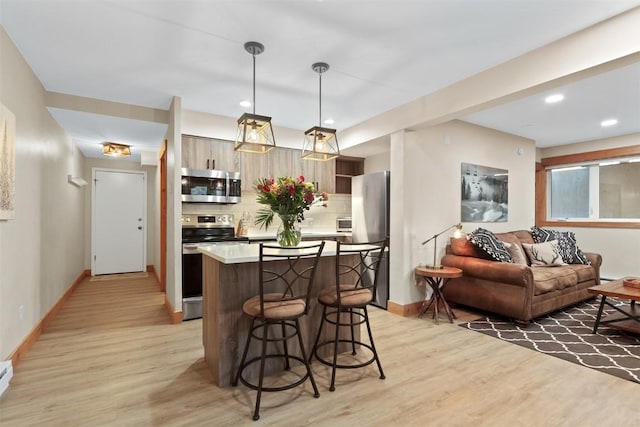kitchen featuring decorative backsplash, a breakfast bar area, stainless steel appliances, light wood-style flooring, and baseboards