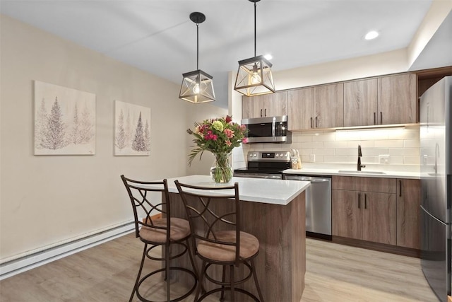 kitchen featuring stainless steel appliances, light countertops, a sink, light wood-style floors, and a kitchen bar
