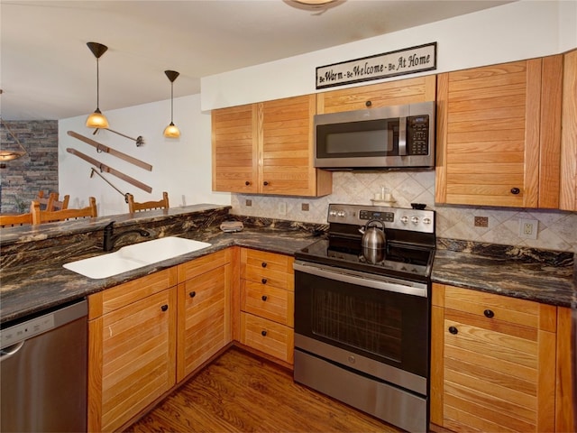 kitchen featuring pendant lighting, sink, dark stone countertops, backsplash, and stainless steel appliances