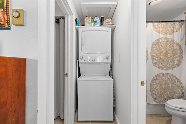 clothes washing area featuring light tile patterned flooring, stacked washing maching and dryer, and laundry area