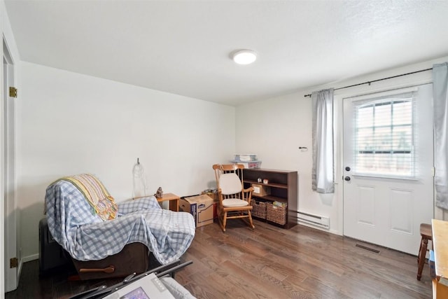 sitting room with a baseboard heating unit, wood finished floors, and visible vents