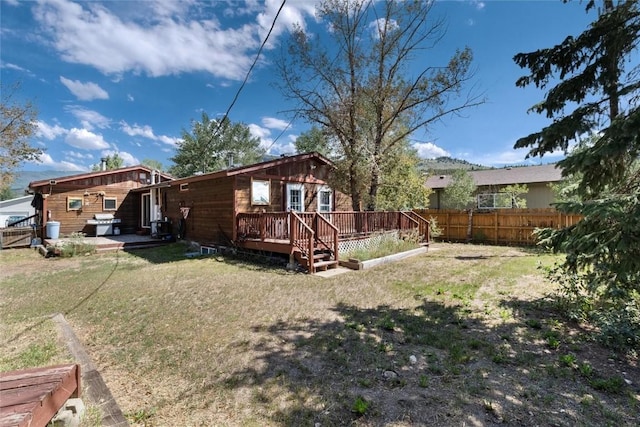 back of property with a lawn, a wooden deck, and fence