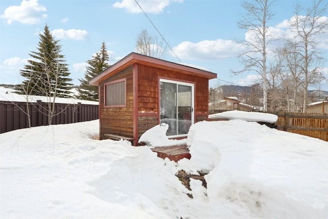 snow covered structure featuring a fenced backyard and an outdoor structure