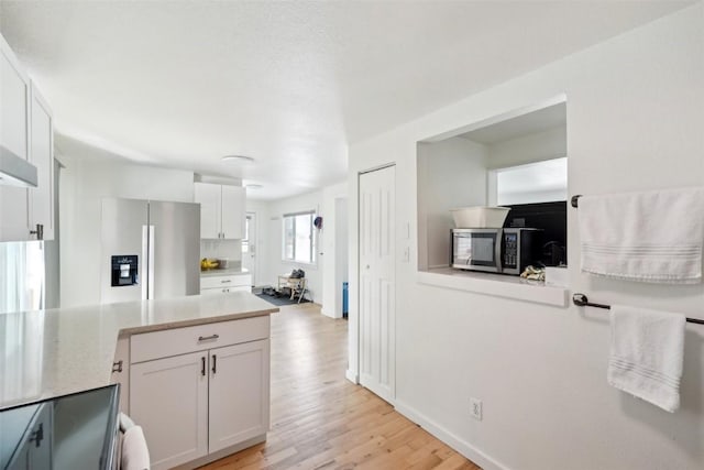 kitchen featuring light wood-style floors, stainless steel appliances, a peninsula, white cabinetry, and light stone countertops