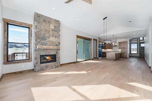 unfurnished living room with a stone fireplace, lofted ceiling, light wood-style floors, and baseboards