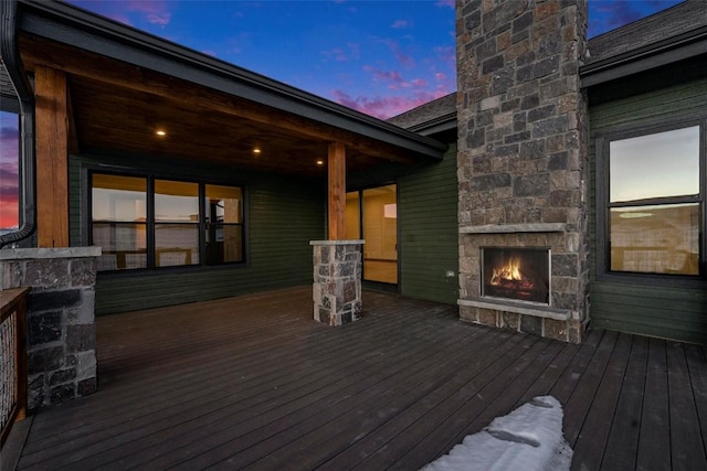 deck at dusk featuring an outdoor stone fireplace