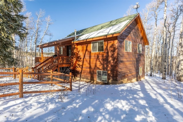 snow covered property with a wooden deck, stairway, and fence