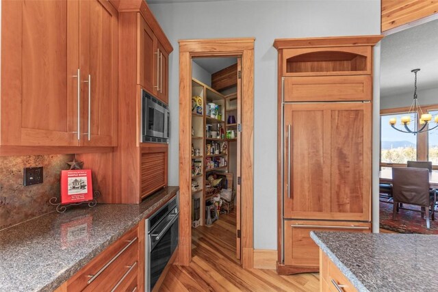 kitchen featuring built in appliances, hanging light fixtures, a notable chandelier, light wood-style floors, and backsplash