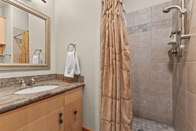 bathroom featuring a textured wall, tiled shower, and vanity