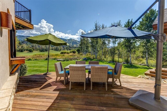 wooden terrace with outdoor dining space, a lawn, and a mountain view