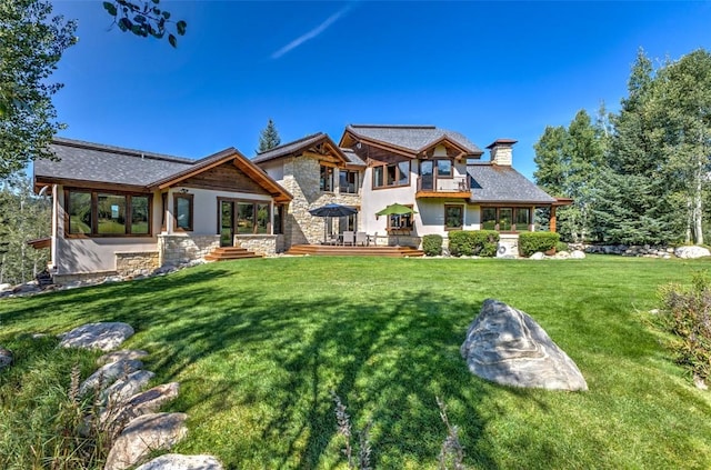 rear view of property featuring a balcony, stone siding, a chimney, and a lawn