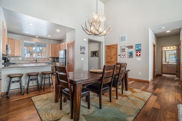 dining area with dark wood-type flooring, a chandelier, sink, and a high ceiling