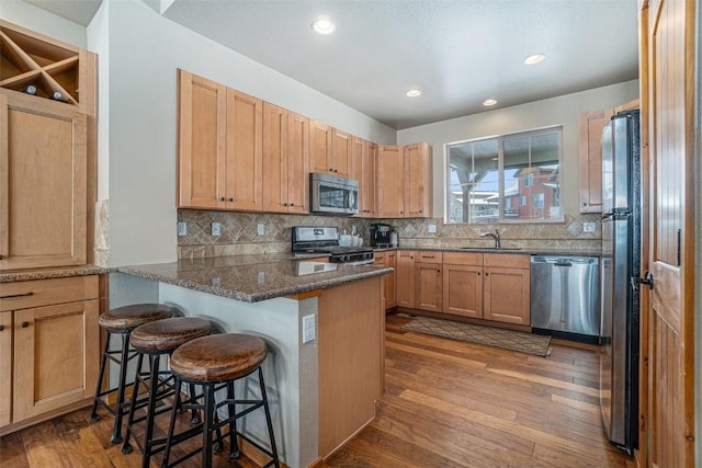 kitchen with sink, a breakfast bar area, dark stone counters, kitchen peninsula, and stainless steel appliances