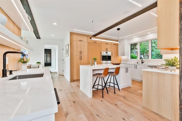 24 Maple St, Steamboat Springs, CO 80487 - kitchen featuring a sink, stainless steel oven, beamed ceiling, light brown cabinets, and a kitchen bar