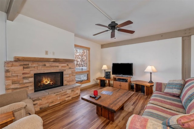 living area featuring wood finished floors, a ceiling fan, and a stone fireplace