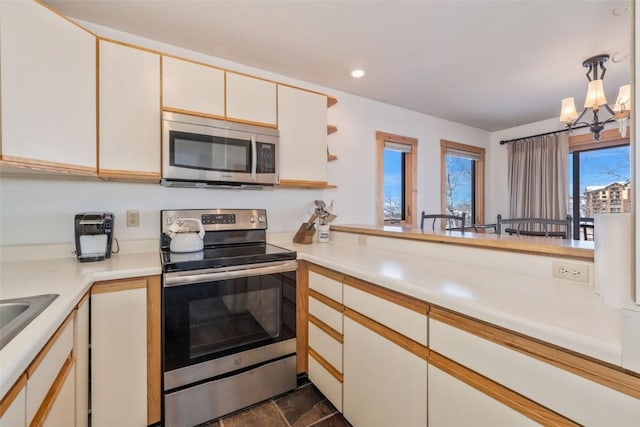 kitchen with stainless steel appliances, light countertops, a chandelier, cream cabinets, and decorative light fixtures