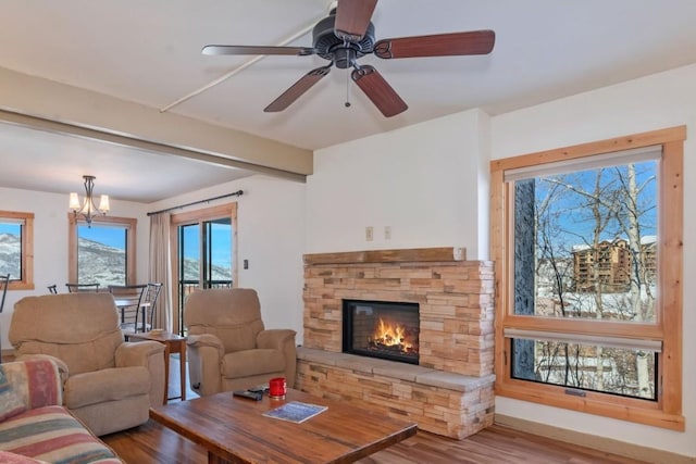 living room featuring a stone fireplace, wood finished floors, beamed ceiling, a chandelier, and ceiling fan