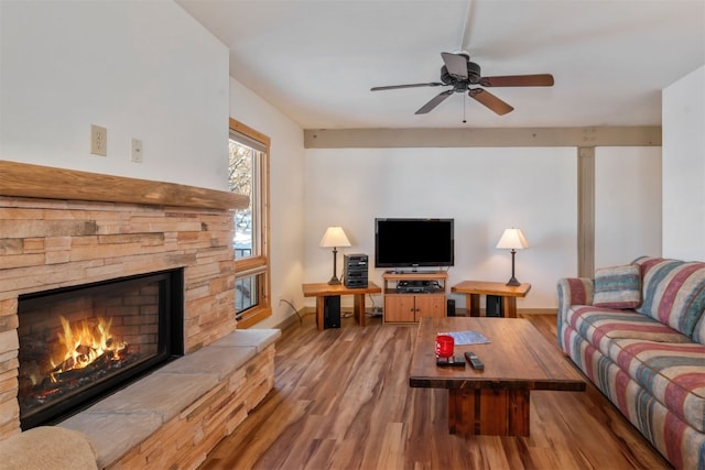 living room with wood finished floors, a stone fireplace, baseboards, and a ceiling fan