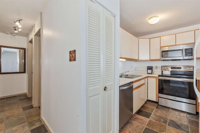kitchen with stainless steel appliances, stone finish flooring, a sink, and light countertops
