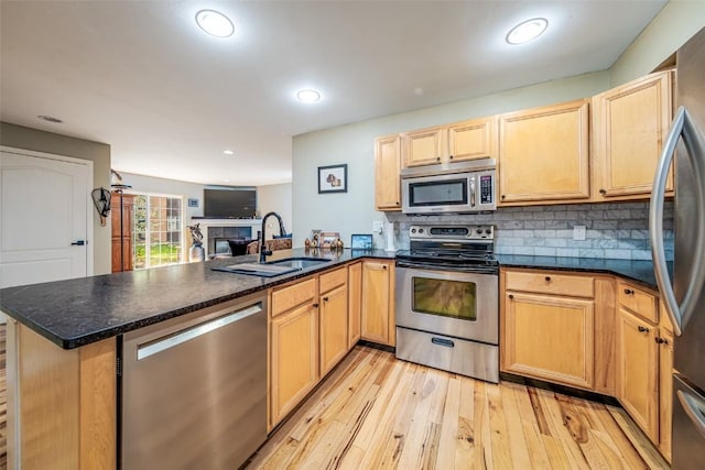 kitchen with a sink, open floor plan, light wood-type flooring, a peninsula, and appliances with stainless steel finishes