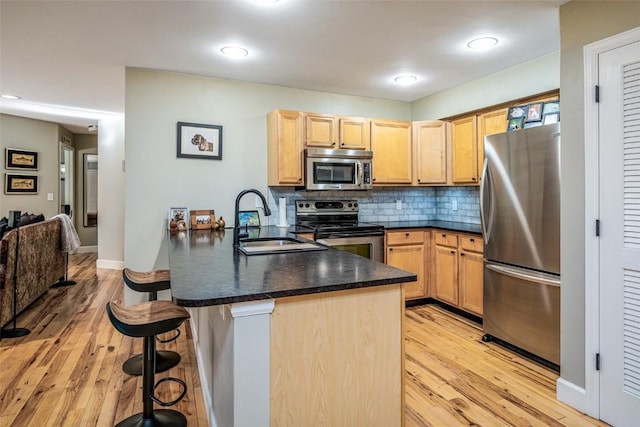 kitchen featuring stainless steel appliances, a peninsula, a sink, dark countertops, and a breakfast bar