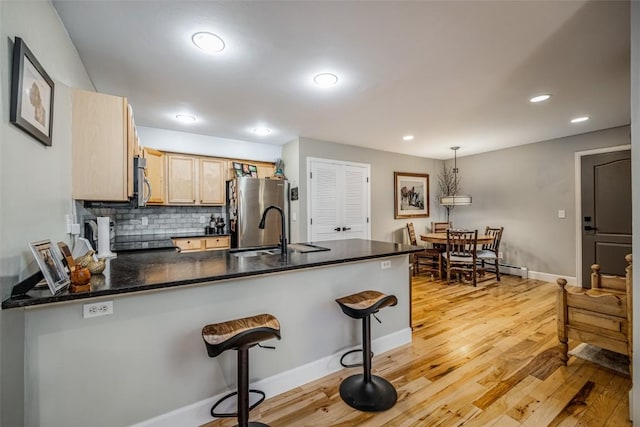 kitchen with decorative backsplash, light wood-style flooring, a kitchen bar, a peninsula, and appliances with stainless steel finishes