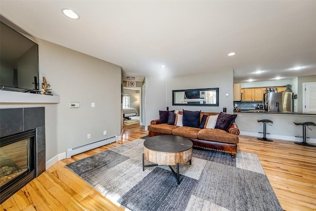 living area with a baseboard heating unit, light wood-style flooring, a tiled fireplace, baseboards, and recessed lighting