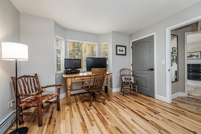 office area with a baseboard radiator, light wood finished floors, and baseboards